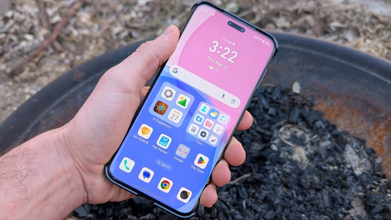 A hand holding a phone over a fire pit.