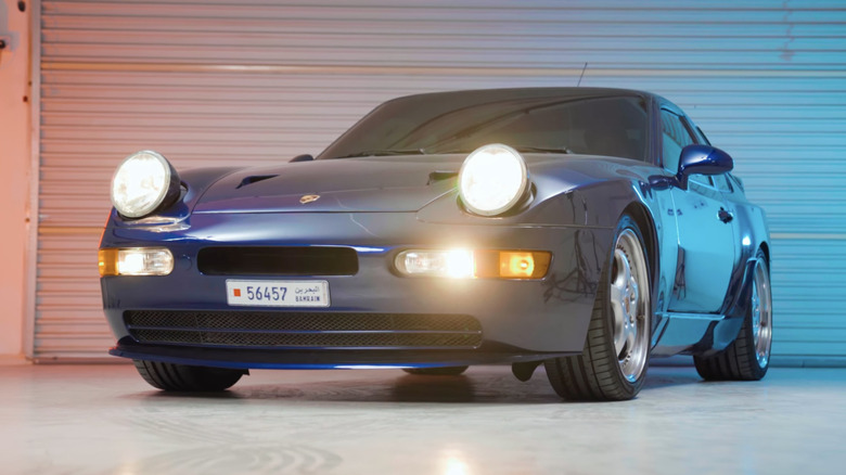 A rare blue Porsche 968 Turbo S photographed from the front under studio lights in a garage.