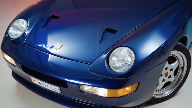 A front-end close-up of a rare blue Porsche 968 Turbo S under studio lights in a garage.