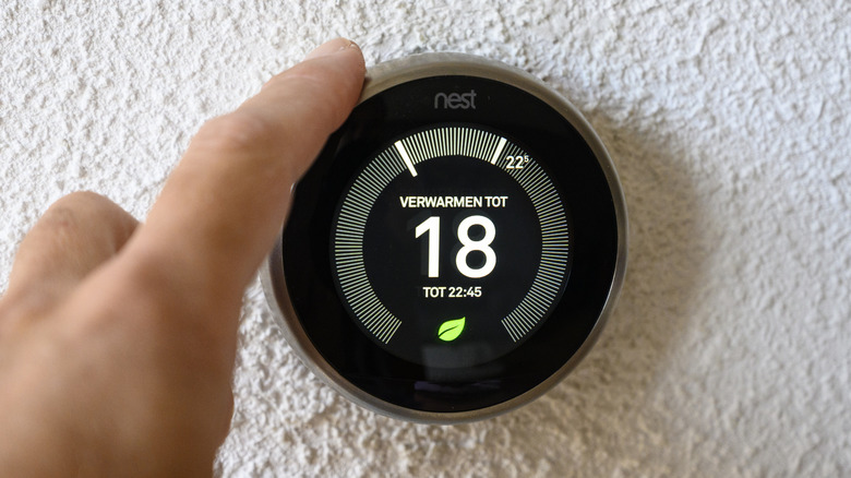 Hand adjusting a Google Nest smart thermostat to adjust the temperature