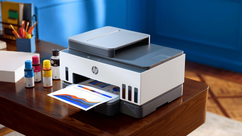 HP Smart Tank 7000 printer on a table next to ink bottles.