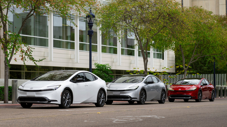 White, silver, and red 2026 Toyota Prius cars parked in a row along a street.