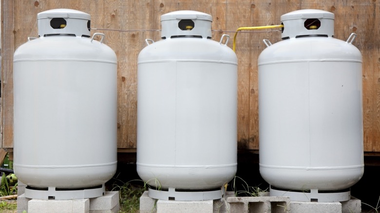Three white propane tanks arranged in a row against a wooden wall