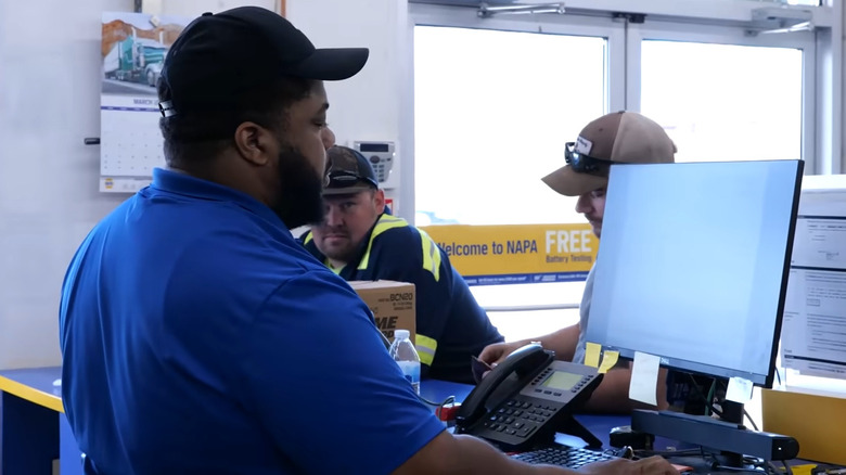Person at the counter of a parts store helping a couple customers