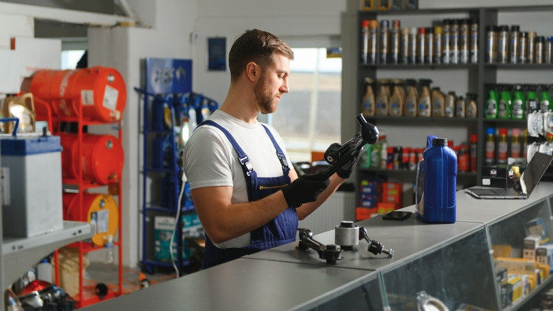 A person at an auto parts store counter is examining a lower control arm