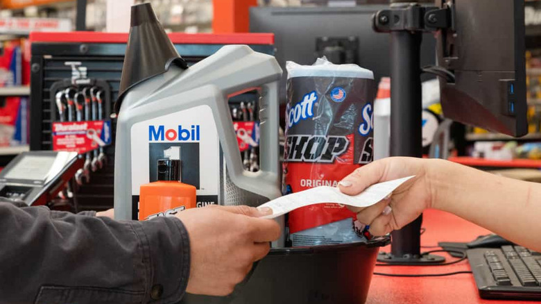 A close-up of a pair of hands exchanging a receipt in front of some oil and other auto products