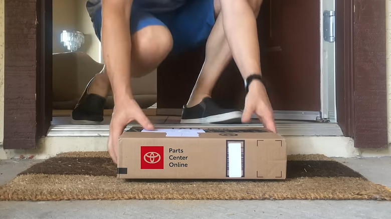 A box labeled Parts Online Center being picked up from a doorstep