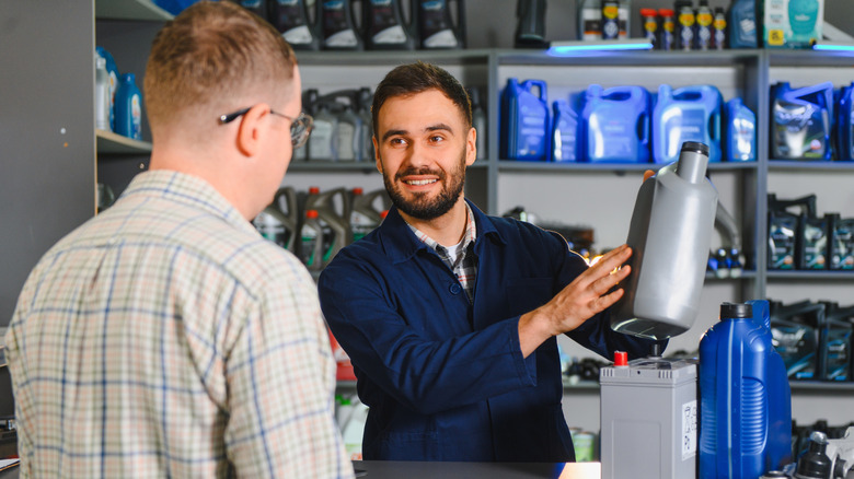 Salesperson offering bottles of oil and battery to customer in parts store