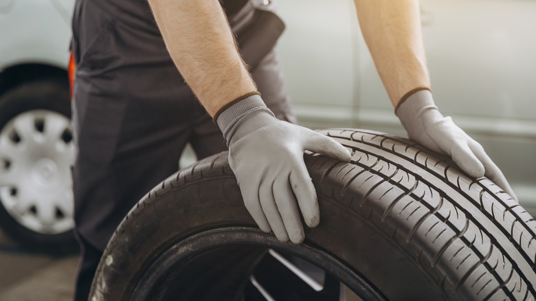 A repair shop worker rolling a replacement tire with his two gloved hands