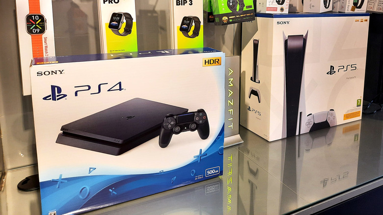 Two PS4s and two PS5s for sale in an electrical shop with smart watches on the wall.