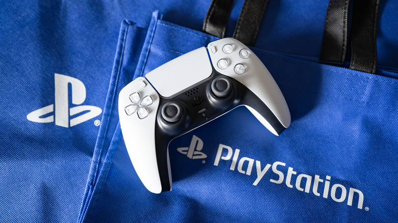 A PlayStation 5 DualSense controller in white on a stack of PlayStation branded shopping bags.