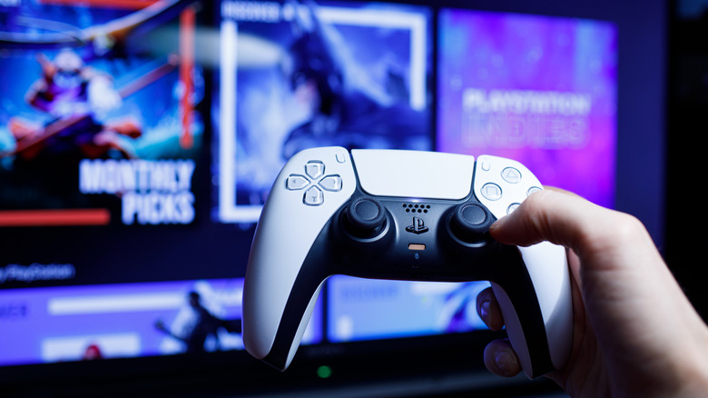 A person holding a PlayStation 5 controller with blurred console display in background