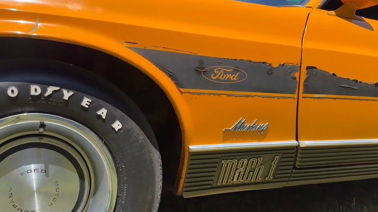 Close-up of 1970 Mustang Mach 1 Twister Special showing front-left quarter panel with peeling decals and "Mustang" and "Mach 1" labels