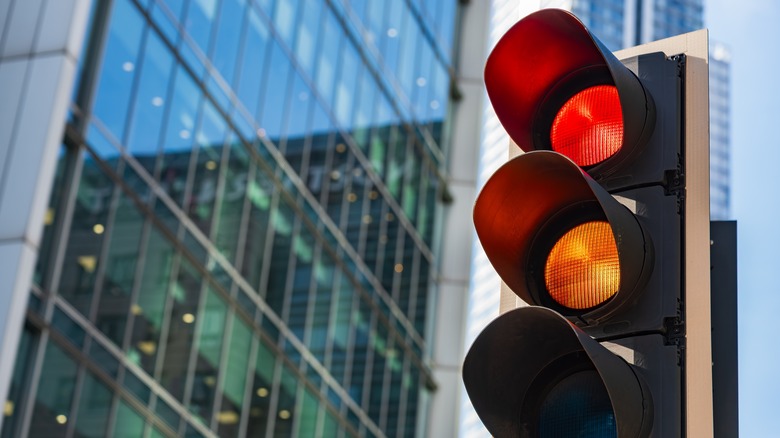 A traffic light turning yellow with modern buildings in the background.