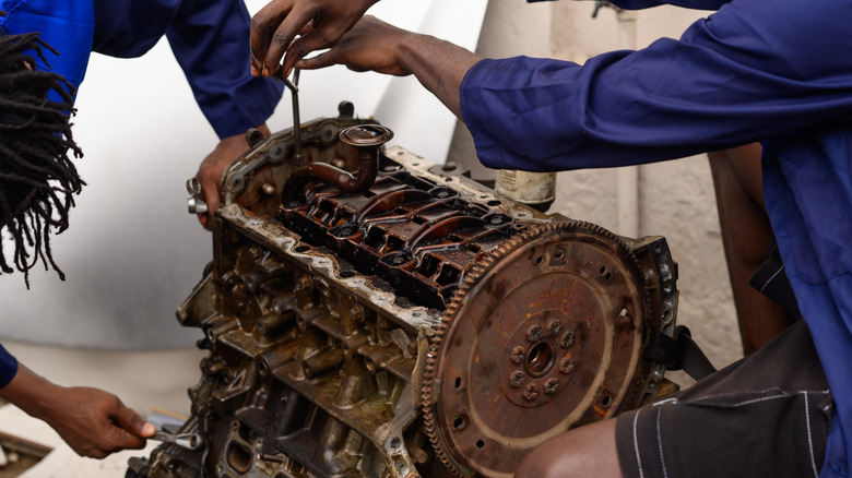 Two mechanics rebuilding a worn-out engiine block, torn down to its base components
