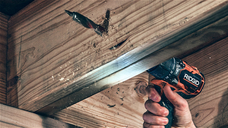 A Ridgid Nuke drill drilling through wood near the ceiling.