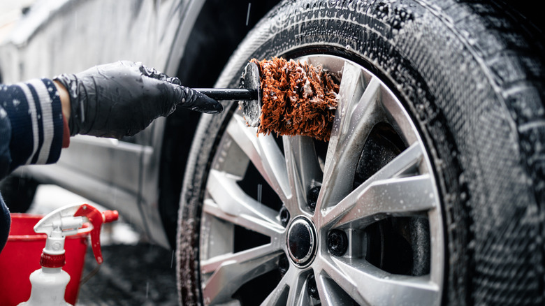 A person wearing black gloves cleaning a wheel of a car