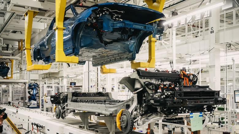 A blue Rivian pickup truck body is hoisted up in factory