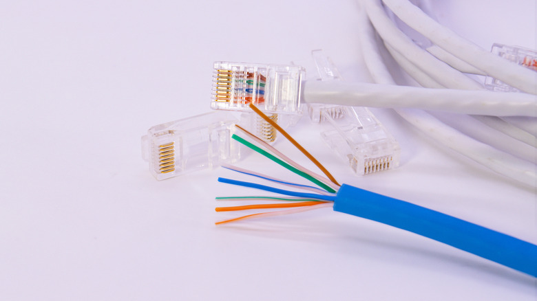 A blue Cat6 Ethernet cable with its eight wires exposed, with a white Ethernet cable and additional two RJ45 connectors placed next to it