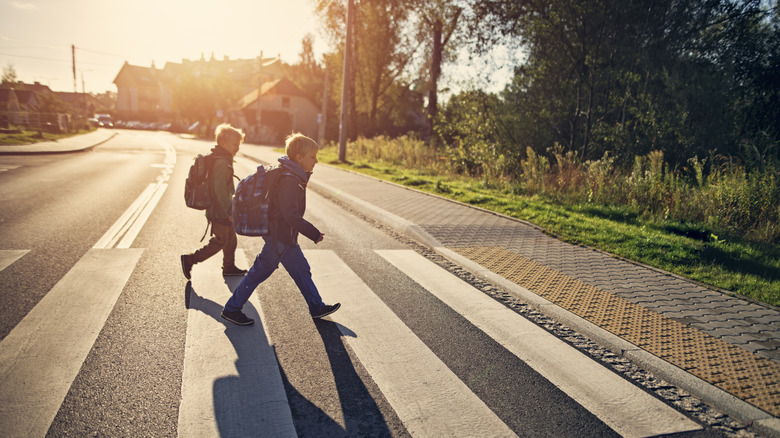Two young boys with backpacks using a crosswalk to cross the street early in the morning