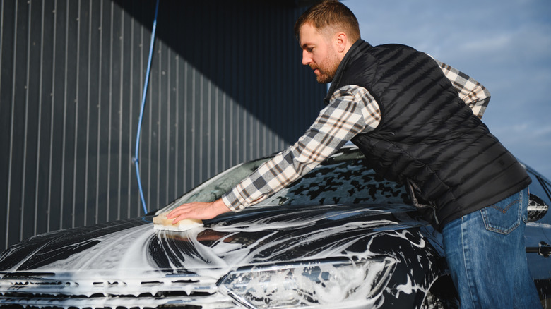 Male worker with a sponge washes a car with foam