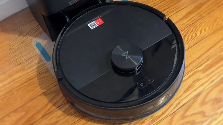 The Roborock Q7 M5+ vacuuming along the wall on a wooden floor.