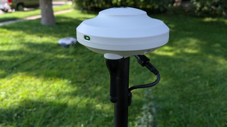 RTK reference station on black pole over green grass.