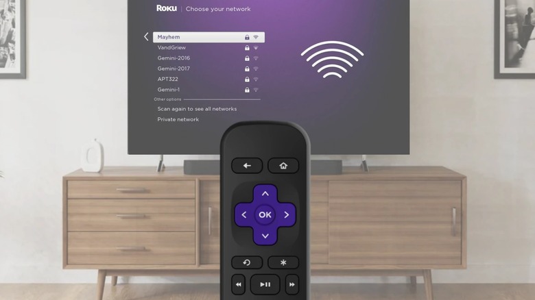 Roku remote in front of TV displaying Roku app settings