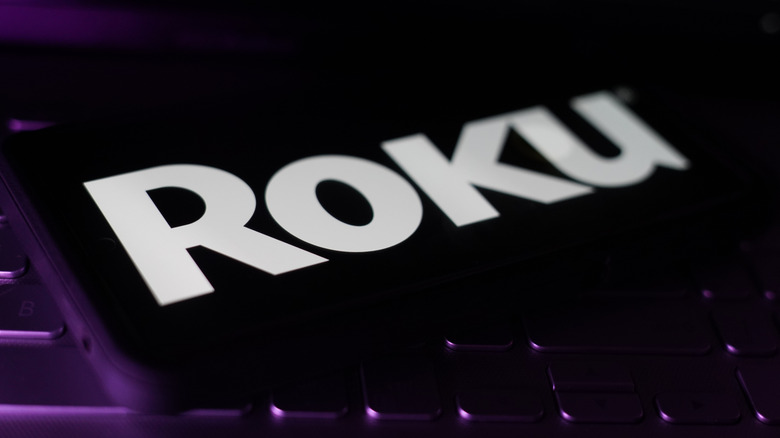 The Roku logo on a screen on a dark and purple-lit image