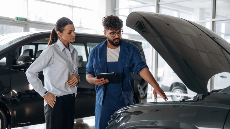 Auto mechanic pointing to engine and explaining something to companion.