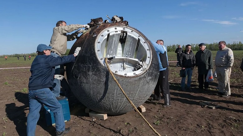 People opening a large, dirty sphere in a field.