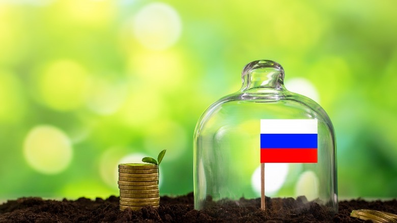 Russian flag under glass jar near coins in dirt