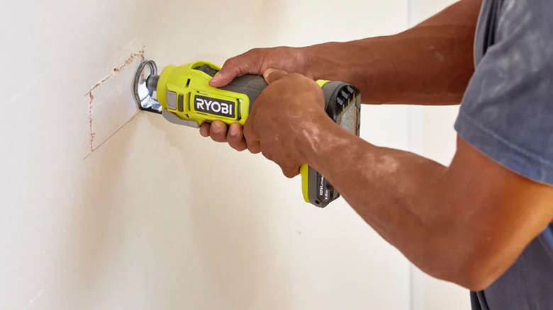 Person holds Ryobi's 18V Cut Out Tool against white wall