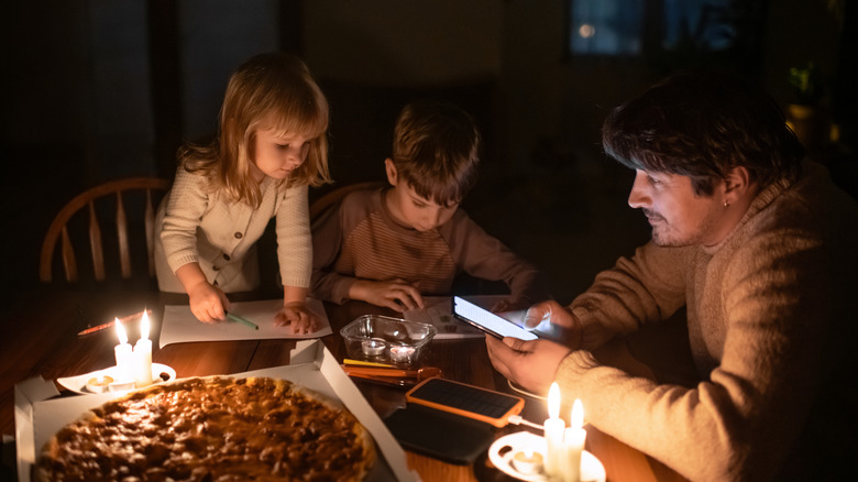 A family sitting around a table during a power outage with candles and a pizza sitting nearby