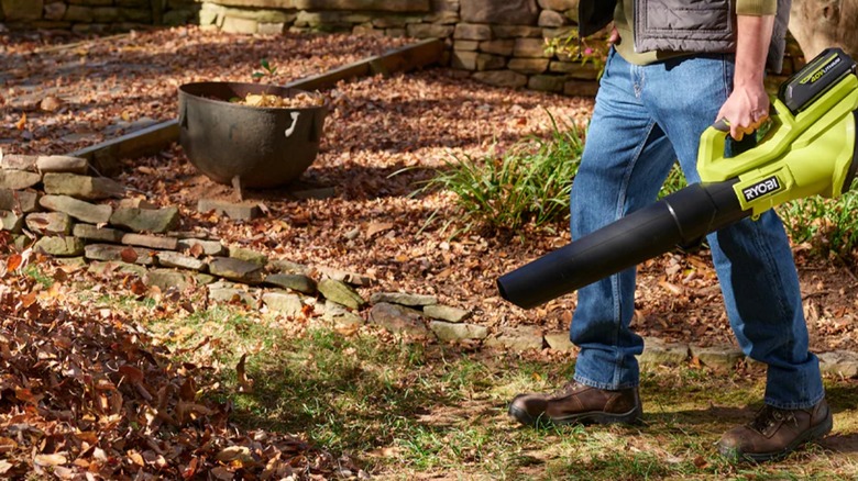 A worker using a 40V Ryobi blower on a leaf pile.