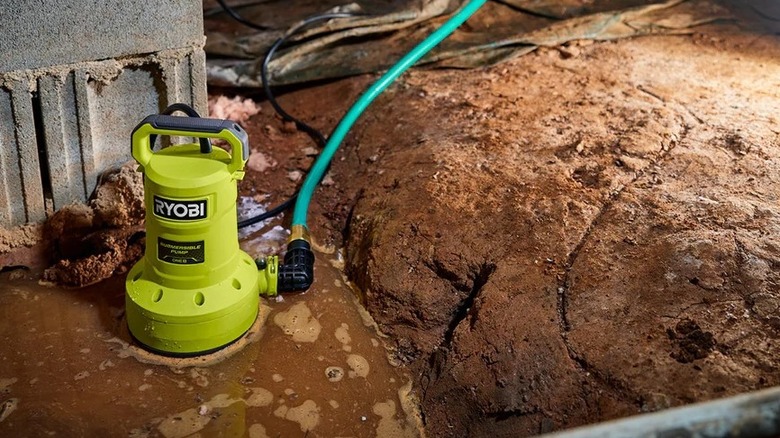 Ryobi submersible pump in a muddy flooded area, with a hose attached