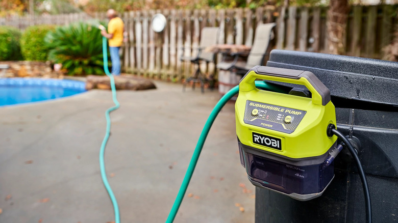 A Ryobi submersible water pump attached to a barrel in a yard