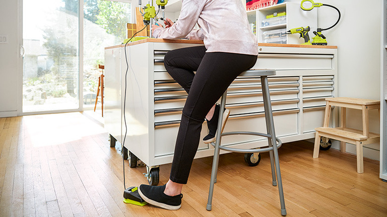 Bottom half of a person on a stool with one foot on a pedal in a craft room