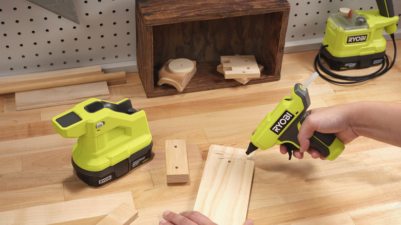 Hand using Ryobi compact glue gun on piece of wood