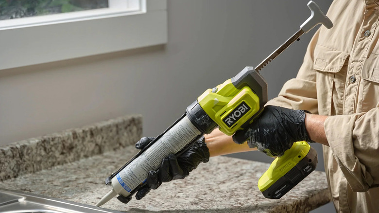 A person using a Ryobi caulk gun to caulk a kitchen sink