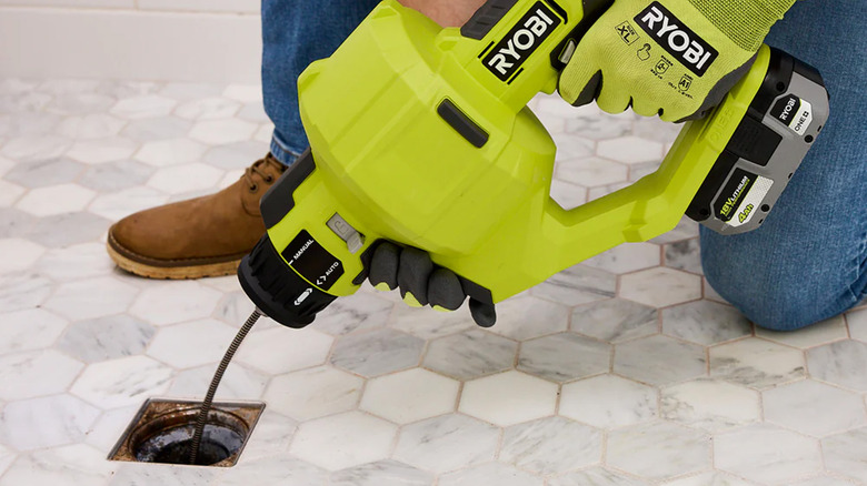 A person unclogging a drain with a Ryobi drain auger