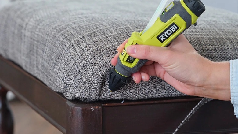 A person using Ryobi USB Lithium Glue Pen to fix chair fabric