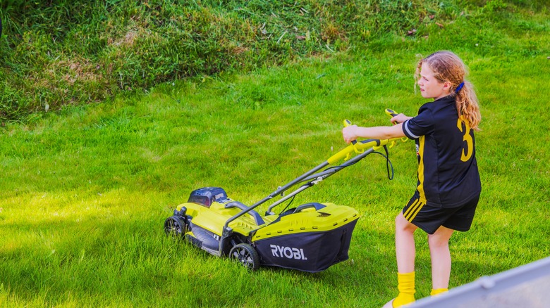 Young girl in soccer uniform cutting grass with Ryobi lawn mower