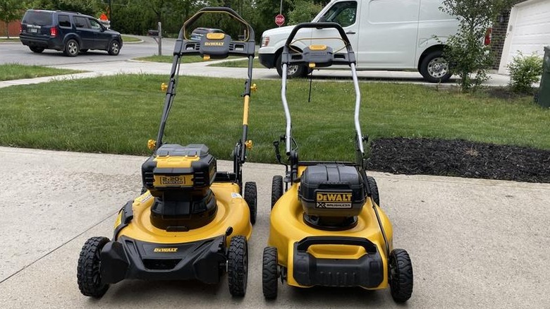 Two DeWalt lawn mowers on sidewalk with vehicles in background