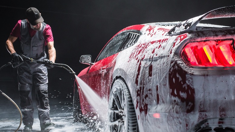 man cleaning red car with pressure washer