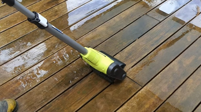 A person cleaning a deck with a Ryobi patio cleaner.