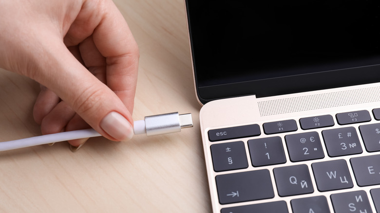 A hand plugging in USB C port into a laptop