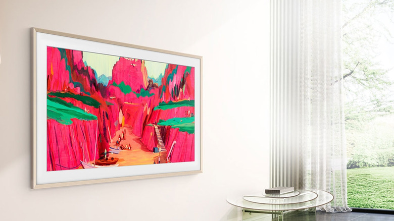 The Frame TV by Samsung, displaying a red and green landscape painting on a cream wall next to a large window