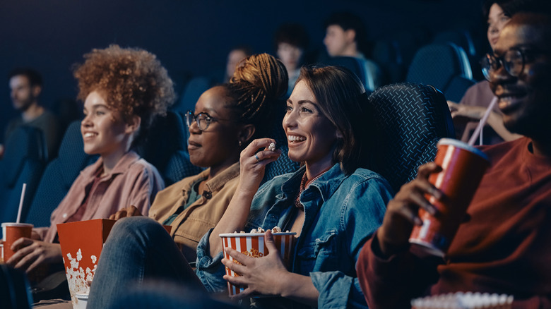 Happy woman eating popcorn while watching movie with her friends in a theater