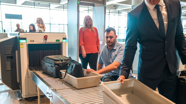 Passengers in line to grab their belongings after baggage screening at an airport checkpoint